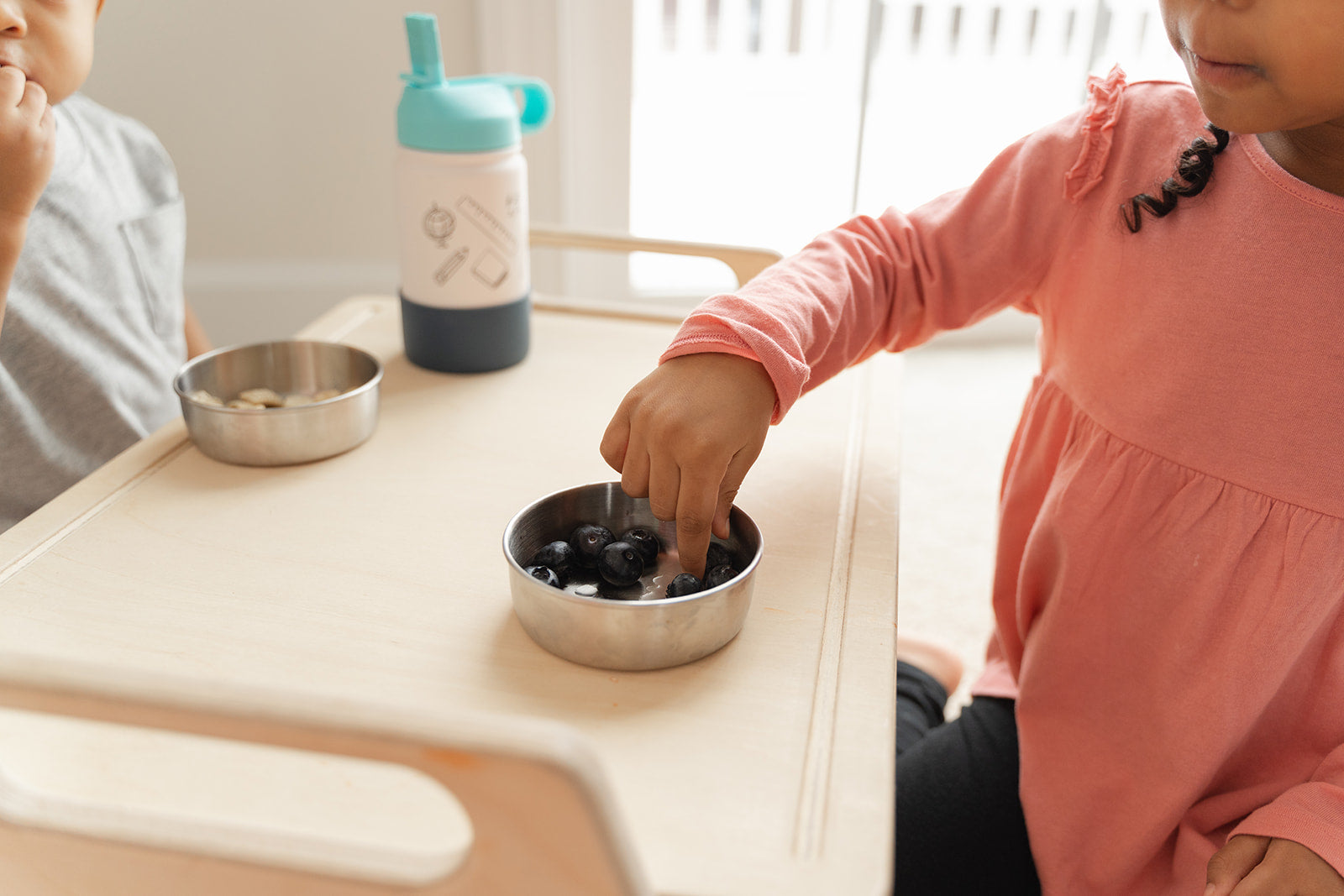 Two toddlers sharing small wooden floor table for parallel play and social interaction, portable activity tray accommodating multiple children for puzzles crafts or snack time, Montessori-inspired play table encouraging cooperation and turn-taking skills in preschool daycare or home playroom environment